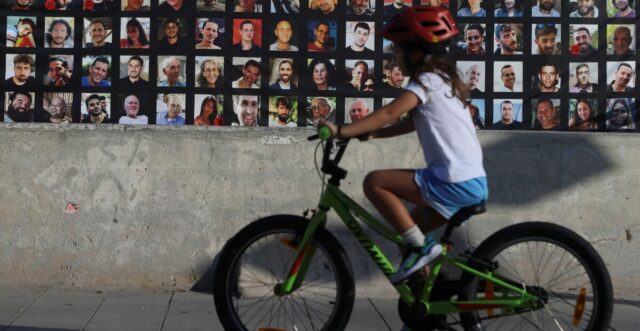 A child rides a bike past images of those taken hostage or killed during the deadly October 7 attac