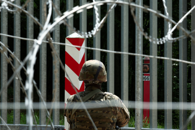 soldier stands guard near the fence on the Belarusian-Polish border