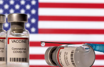 Vials labelled "VACCINE Coronavirus COVID-19" and a syringe are seen in front of a displayed US flag in this illustration taken December 11, 2021. REUTERS/Dado Ruvic/Illustration