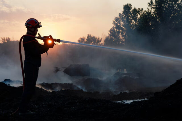 4YPKEO4D7VMZZBZ7JPJNJTL7CE A firefighter is silhouetted while conducting a water rescue operation at sunset amid land scorched by a wildfire near Saint-Laurent-de-la-Cabrerisse, southern France, August 7, 2025. REUTERS/Manon Cruz