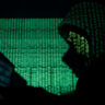 A hooded man holds a laptop computer as cyber code is projected on him in this illustration picture taken on May 13, 2017. REUTERS/Kacper Pempel/Illustration/FIle Photo
