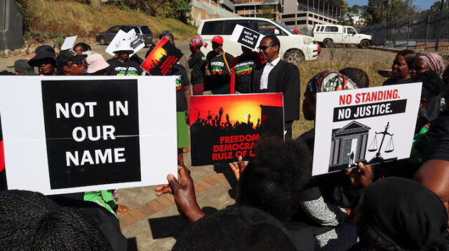 GPIJ5447XJIBHHEY36VFO6X6CY Protesters hold placards as lead applicant and lawyer Mzwandile Masuku addresses them outside the court, after a hearing was postponed, in Mbabane, Eswatini, August 22, 2025. REUTERS/Zakhele Mabuza