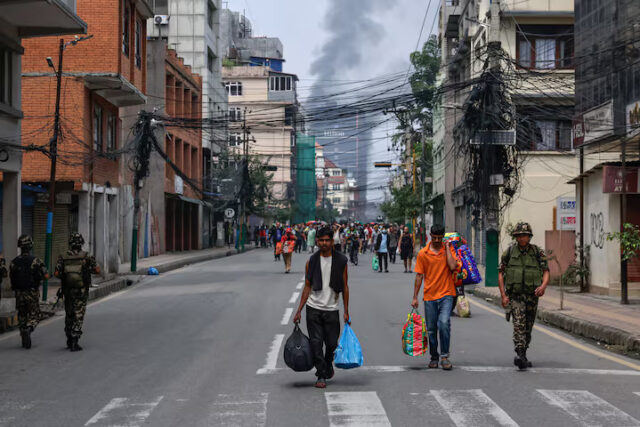 L3BH7XOA2BPC3PEDFFVTTLL53U Smoke rises from the burnt Hilton Kathmandu hotel in the distance as prisoners carrying belongings walk back to Dilli Bazaar jail, next to a soldier, after escaping and being sent back by the Nepalese army, following protests against Monday's killing of 19 people after anti-corruption protests triggered by a social media ban which was later lifted, in Kathmandu, Nepal, September 10, 2025. REUTERS/Navesh Chitrakar