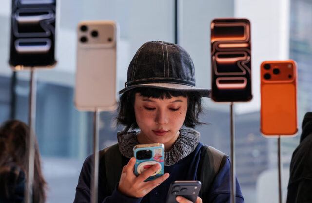PX56YHXH4JIOVF7PWQG4SBEBEA A woman uses her smartphone inside the Apple store in Beijing's Sanlitun area as the new iPhone 17 series smartphones go on sale in Beijing, China September 19, 2025. REUTERS/Maxim Shemetov/File Photo