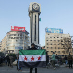 A man holds a Syrian opposition flag near the clock tower in Homs after Syria's army command notified officers on Sunday that President Bashar al-Assad's 24-year authoritarian rule has ended, a Syrian officer who was informed of the move told Reuters, following a rapid rebel offensive, in Homs, Syria December 8, 2024. REUTERS/Mahmoud Hasano