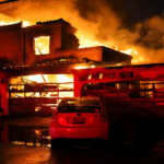 Smoke and flames rise from a burning home, as powerful winds fueling devastating wildfires in the Los Angeles area force people to evacuate, in Malibu, California, U.S. January 8, 2025. REUTERS/Daniel Cole