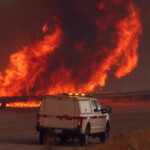 A vehicle drives by as smoke and flames rise in the back while firefighters battle the Hughes Fire near Castaic Lake, north of Santa Clarita, California, U.S. January 22, 2025. REUTERS/David Swanson