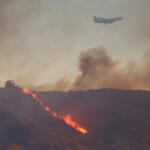 An aircraft flies overhead a heavy machinery battling the Hughes Fire in Castaic Lake, California, U.S. January 22, 2025. REUTERS/David Swanson