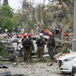 Rescue personnel stand next to damaged vehicles as they work at an impact site following missile attack from Iran on Israel, in Rishon LeZion, Israel, June 14, 2025. REUTERS/Ronen Zvulun