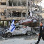 An Israeli police officer walks past damaged vehicles at an impact site following missile attack from Iran on Israel, in Ramat Gan, Israel, June 14, 2025. REUTERS/Ronen Zvulun