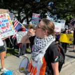 A person uses a megaphone as protesters hold signs as they take part in a "No Kings" protest against U.S. President Donald Trump's presidency and immigration policies, near Mar-a-Lago, in West Palm Beach, Florida, U.S., June 14, 2025. REUTERS/Julien Pretot