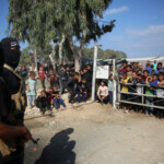 Palestinian Hamas militants stand guard as people gather to watch Red Cross vehicles transport hostages, held in Gaza since the deadly October 7, 2023 attack, following their handover as part of a ceasefire and hostages-prisoners swap deal between Hamas and Israel, in the central Gaza Strip, October 13, 2025. REUTERS/Stringer
