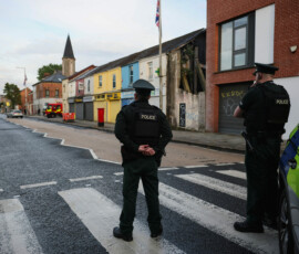 Police officers stand guard as smoke billows from a burning vehicle during a protest after a knife attack on June 8 left a man seriously injured and prompted police to declare a critical incident, on Newtownards Road in Belfast, Northern Ireland, June 9, 2026. REUTERS/Isabel Infantes