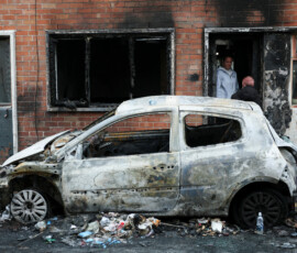 A woman speaks to a person from the doorway of her burnt house, as a destroyed car stands on the street, in the aftermath of anti-immigrant protests following a knife attack on June 8, which left a man seriously injured and prompted police to declare a critical incident, in Belfast, Northern Ireland, June 10, 2026. REUTERS/Isabel Infantes