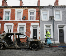 A worker picks debris scattered on the street next to a burnt car, in the aftermath of anti-immigrant protests following a knife attack on June 8, which left a man seriously injured and prompted police to declare a critical incident, at Lendrick Street, east Belfast, Northern Ireland, June 10, 2026. REUTERS/Isabel Infantes