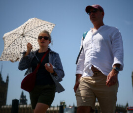 A woman uses an umbrella to shield herself from the sun as she walks on Westminster Bridge, near the Houses of Parliament, amid hot weather in London, Britain, June 23, 2026. REUTERS/Guglielmo Mangiapane