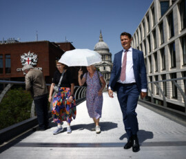 A woman walks with an umbrella along the Millennium Bridge as Britain experiences record temperatures disrupting schools and transport networks in London, Britain, June 23, 2026. REUTERS/Jack Taylor