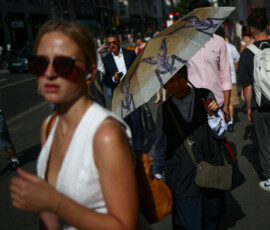A woman uses an umbrella to shield herself from the sun while walking on Oxford Street as Britain experiences record temperatures disrupting schools and transport networks, in London, Britain, June 23, 2026. REUTERS/Guglielmo Mangiapane