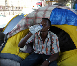 A migrant drinks water in front of his tent at a makeshift camp set up under an elevated railway of a Paris metro line near the Stalingrad subway station, as temperatures rise in paris during a heatwave affecting a large part of France, June 24, 2026. REUTERS/Abdul Saboor