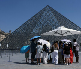 Tourists stand under umbrellas to protect themselves from the sun in front of the glass Pyramid of the Louvre museum as the museum closes early due to the heatwave as temperatures rise in Paris, France, June 24, 2026. REUTERS/Alice Sacco
